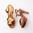 Copper snake print platform sandals for women, two copper-bronze metallic snake-embossed bands cross over the vamp above a thick covered platform, fastened at the ankle by a rose-gold pin buckle, with a mirror-gold footbed and a nude-lacquered inner shank showing behind a tall tapering cone heel in matching copper snake