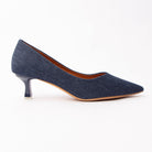 Navy blue denim kitten heels for women, an indigo denim pointed court with the woven twill grain showing across the vamp, on a glossy navy kitten heel tipped with a clear block over a natural tan sole edge