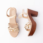 Beige studded platform heels for women, three slim cream croc-embossed straps cross the vamp under a scatter of gold pyramid and round dome studs, held by an elasticated cream ankle loop, over a tan leather-look footbed set on a wood-grain platform and matching wood-grain block heel