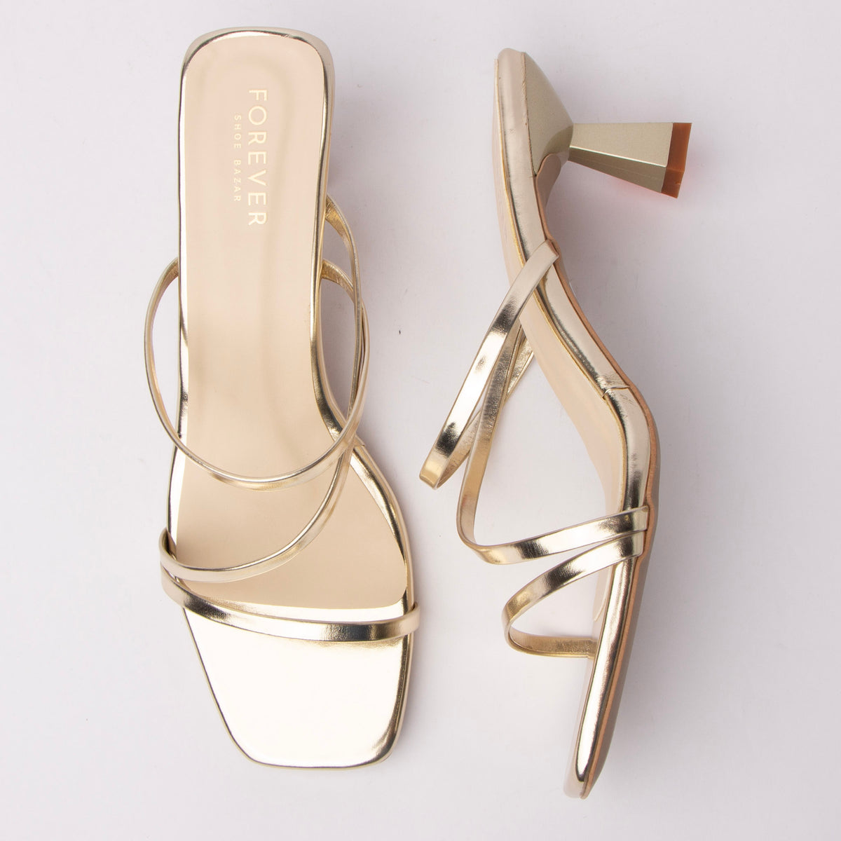 Gold kitten heel mules for women, two slim tubular metallic straps crossing asymmetrically over the vamp, a squared-off toe with a mirror footbed edge, and a sculpted flared hourglass heel in a soft matte finish