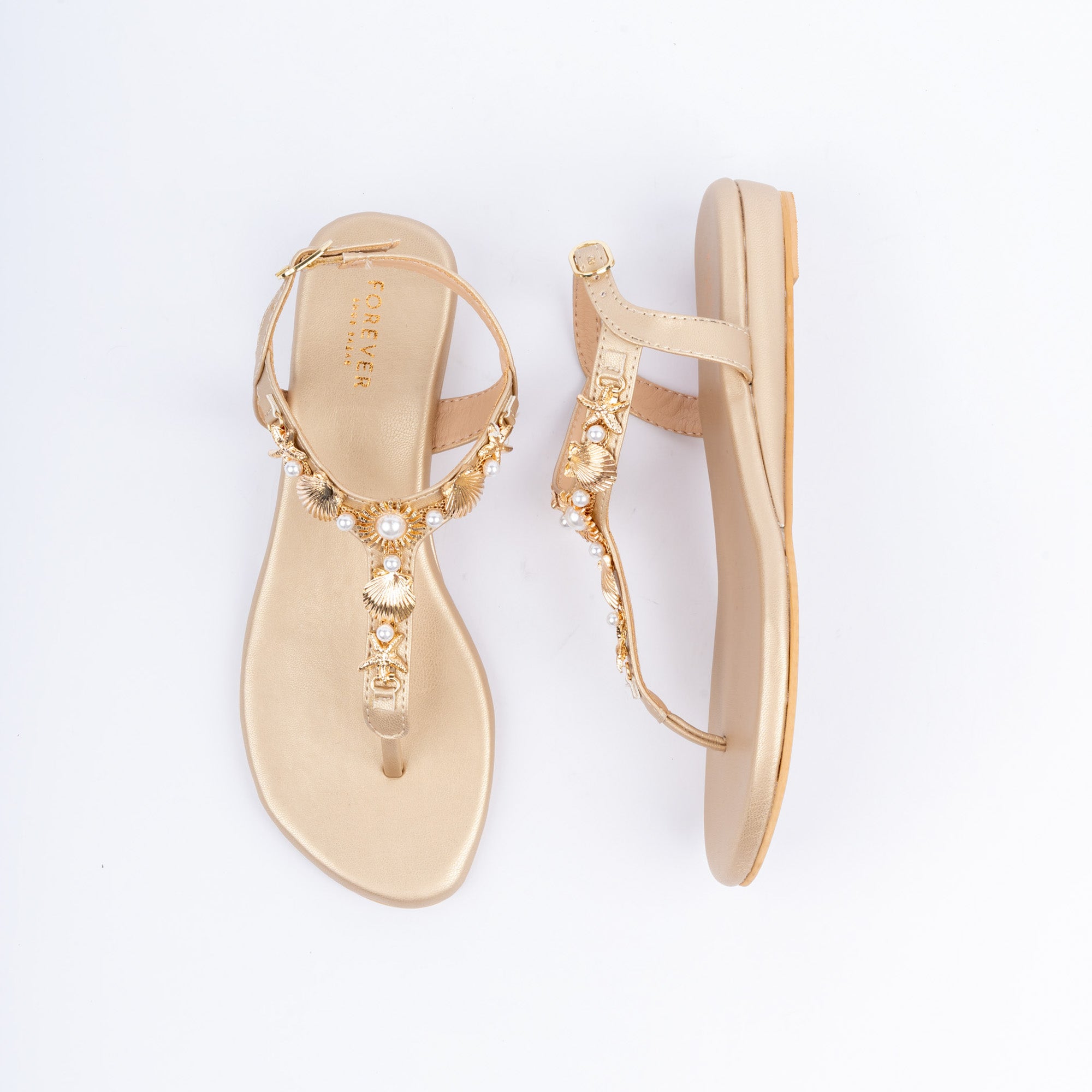 Gold flat sandals for women, gold seashell and starfish charms clustered with pearls along the T-bar, a slim toe post below and a fine ankle strap closed by a small gold buckle, on a cushioned metallic footbed