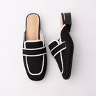 Black knit loafer mules for women, a black knitted-mesh loafer mule outlined in white contrast piping, with an elasticated saddle band across the squared toe and a low black block heel ringed with a gold metal trim over a nude padded footbed
