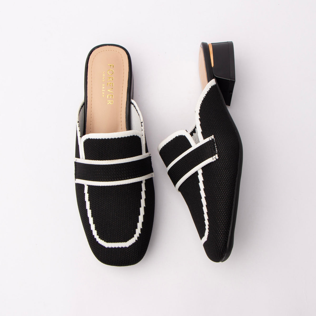 Black knit loafer mules for women, a black knitted-mesh loafer mule outlined in white contrast piping, with an elasticated saddle band across the squared toe and a low black block heel ringed with a gold metal trim over a nude padded footbed