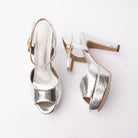 Silver peep toe platform heels for women, bright mirror-silver snake-embossed vamp band with a narrow ankle strap closing on a gold-tone pin buckle that reads as a deliberate warm-on-cool contrast, over a covered toe platform and flared block heel, with a silver footbed, tan lining visible inside the strap and a taupe-nude sole edge