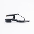 Black block heel sandals for women, a slim T-bar running from a single toe band up to a gold pin-buckle ankle strap, glossy straps on a squared-off footbed and a low block heel