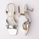 Silver kitten heel sandals for women, snake-embossed metallic straps crossing over the vamp, an ankle strap with a hidden elastic gore for slip-on ease, and a sculpted flared hourglass heel above a mirror-finish footbed