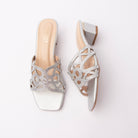 Silver cut out block heel mules for women, a single cut-work vamp band in bright silver metallic pu, its interlaced loops packed edge to edge with clear glass stones for a high-glitter finish, running over a nude footbed and finishing in a silver-covered low block heel with an open back