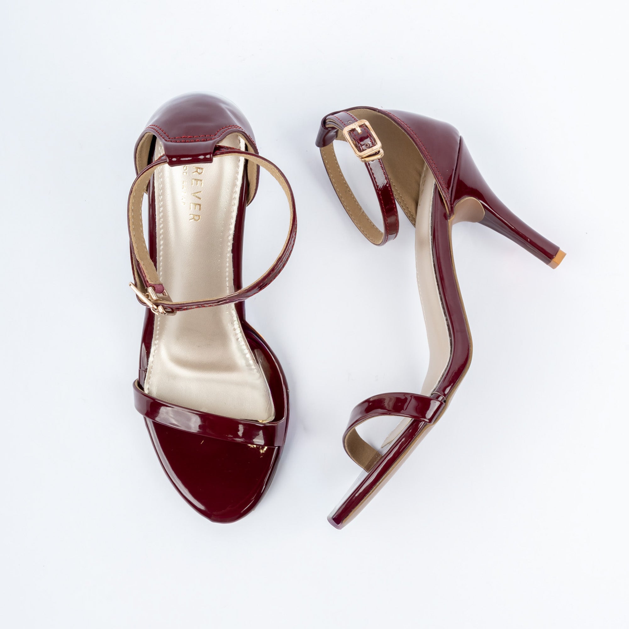 Maroon stiletto heel sandals for women, a single high-gloss toe band over a nude footbed, with a gold square pin-buckle ankle strap and a covered heel counter running into a slim stiletto