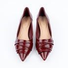 Maroon pumps for women, three overlapping pleated bands fanning diagonally across the vamp and narrowing into a sharp point, over a nude cushioned footbed with a flared kitten heel and clear tip