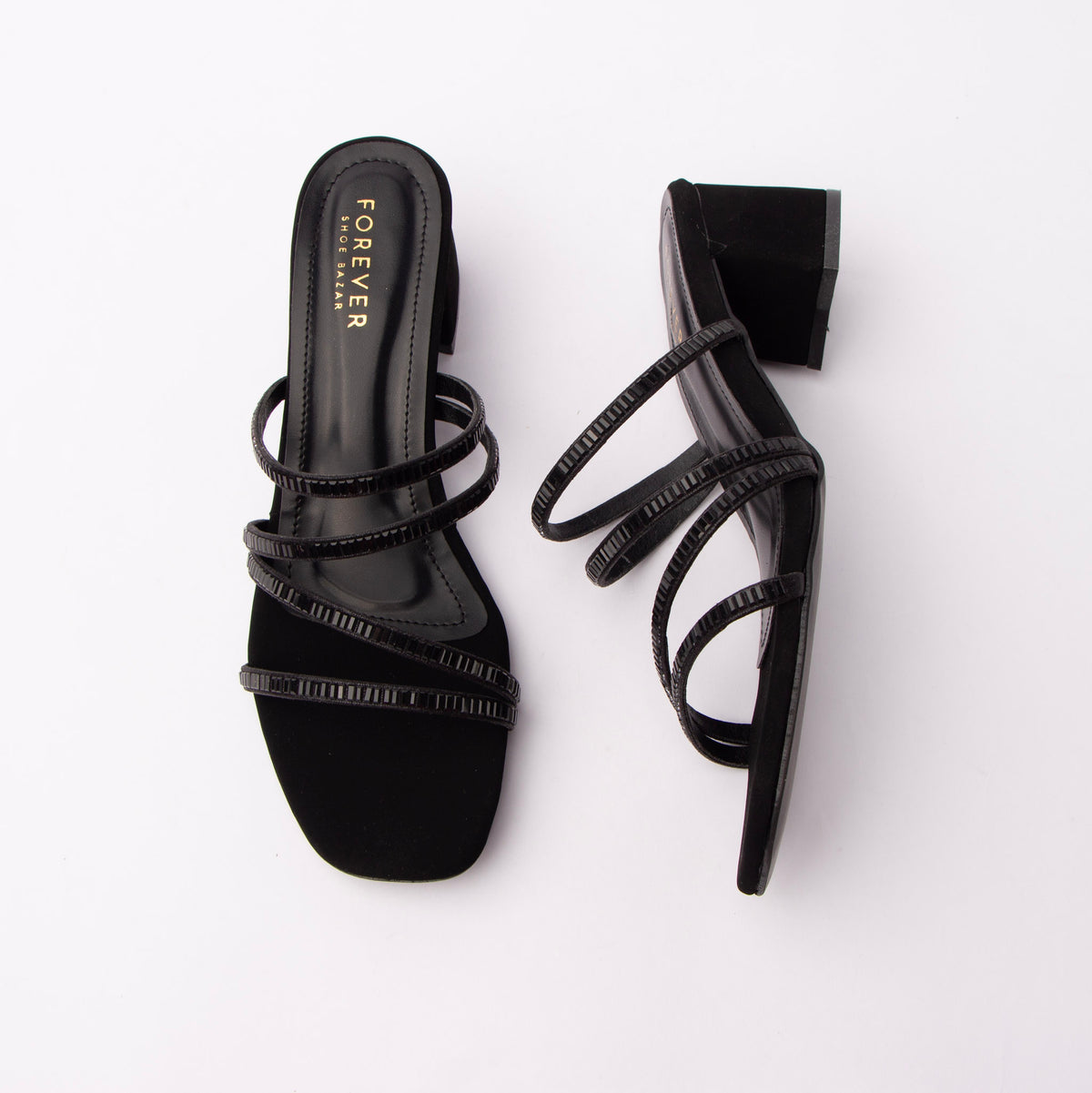 Black criss cross strap mules for women, four slim tubular straps criss-cross the vamp, each one paved end to end with tiny jet-black baguette-cut stones, set against a matte black suede toe band and heel while the footbed and side walls are glossy black patent, and the straight square block heel is suede-covered with a thin black sole edge