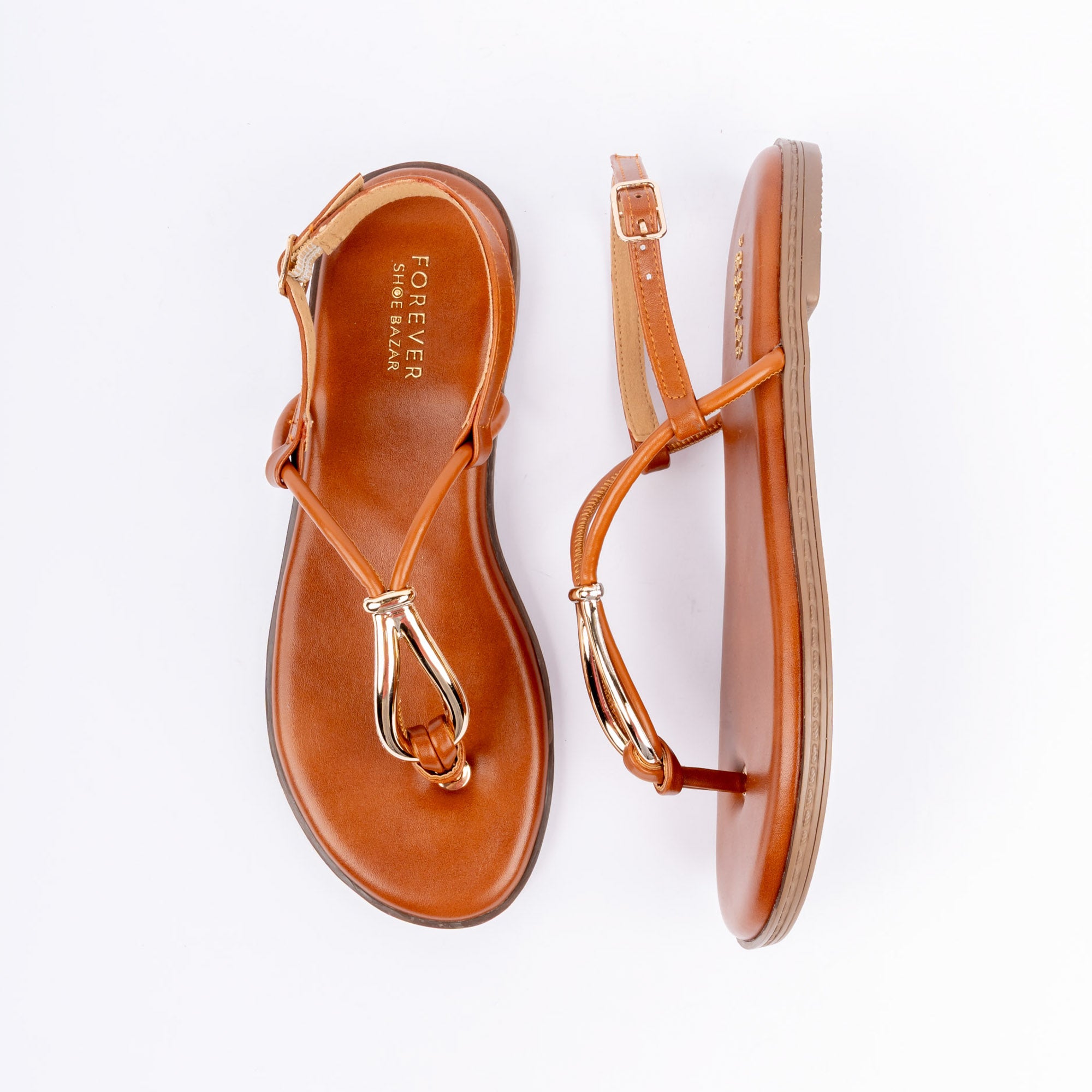 Tan flat sandals for women, a slim toe-post threaded through a polished gold teardrop loop, running into an angled T-strap that meets a pin-buckle backstrap, over a cushioned footbed