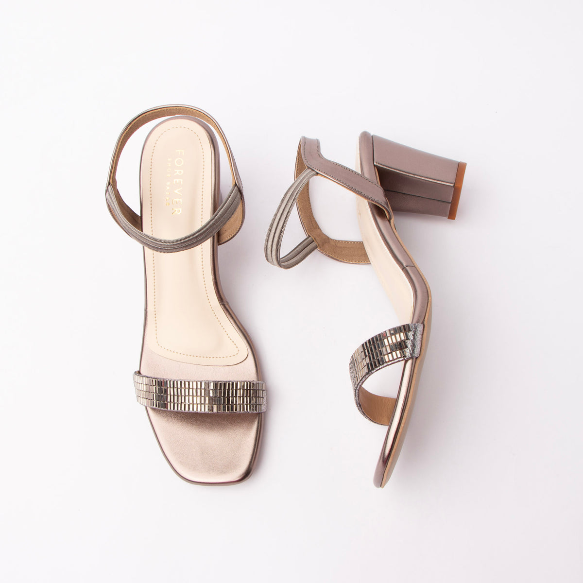 Grey embellished block heel sandals for women, a warm pewter metallic upper with the wide toe band set in rows of gunmetal square stones and a piped pewter sling strap that stretches over the heel on an elastic gore, a cream footbed, and a flared block heel in a soft matte mauve-grey that sits a shade lighter than the shiny upper
