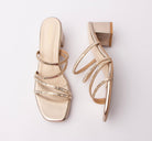 Gold criss cross strap mules for women, a four-strap criss-cross vamp in champagne gold mirror-finish pu, with mirror-cut rectangular stones running the length of every strap so they catch light like a bracelet, over a cream leatherette footbed carrying the gold Forever logo and a square block heel clad in matching gold metallic