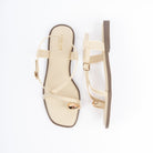 Cream flat sandals for women, a gold dome stud crowning the toe ring, a slim diagonal strap crossing the vamp and a wide backstrap fastened by a small gold pin buckle, on a cushioned footbed