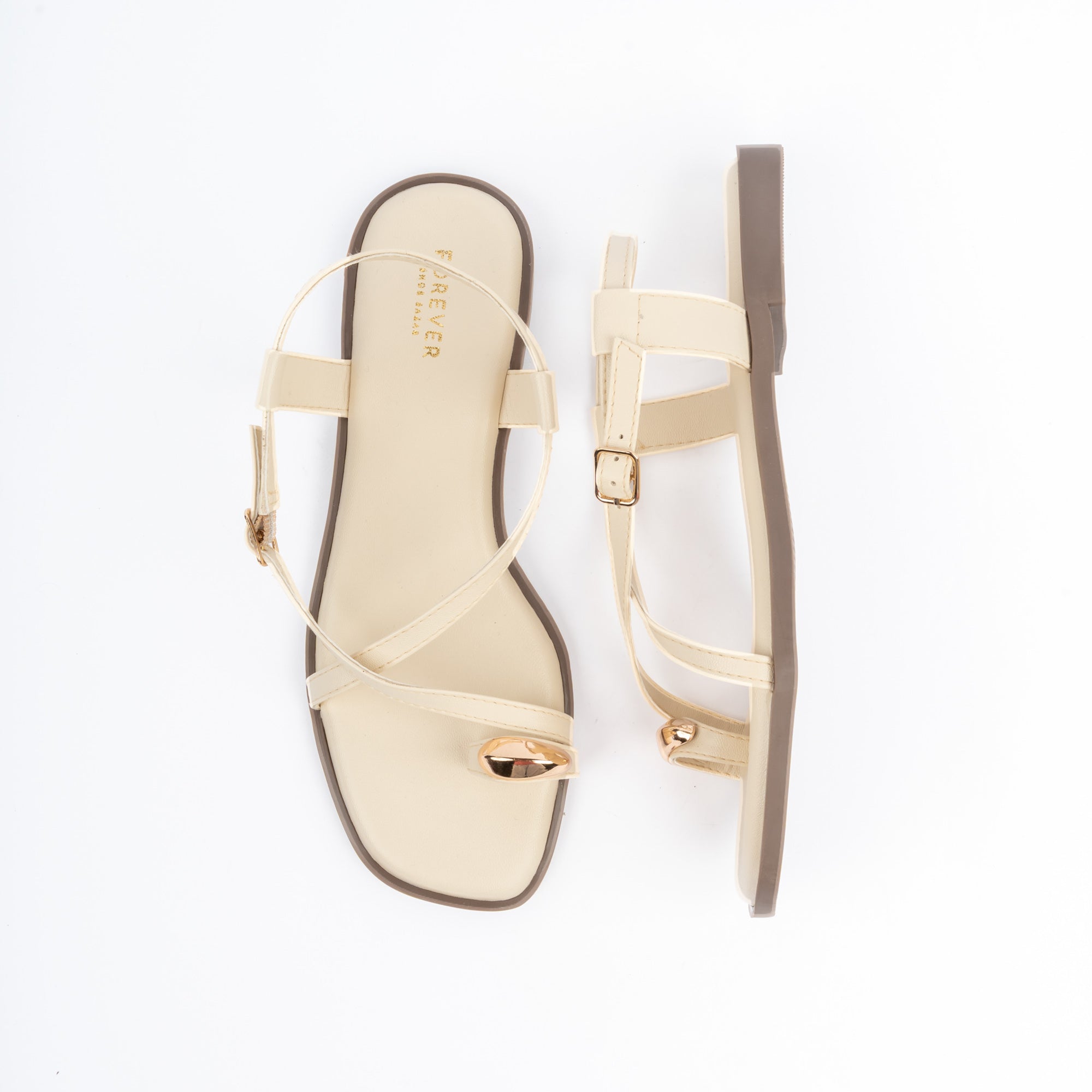 Cream flat sandals for women, a gold dome stud crowning the toe ring, a slim diagonal strap crossing the vamp and a wide backstrap fastened by a small gold pin buckle, on a cushioned footbed