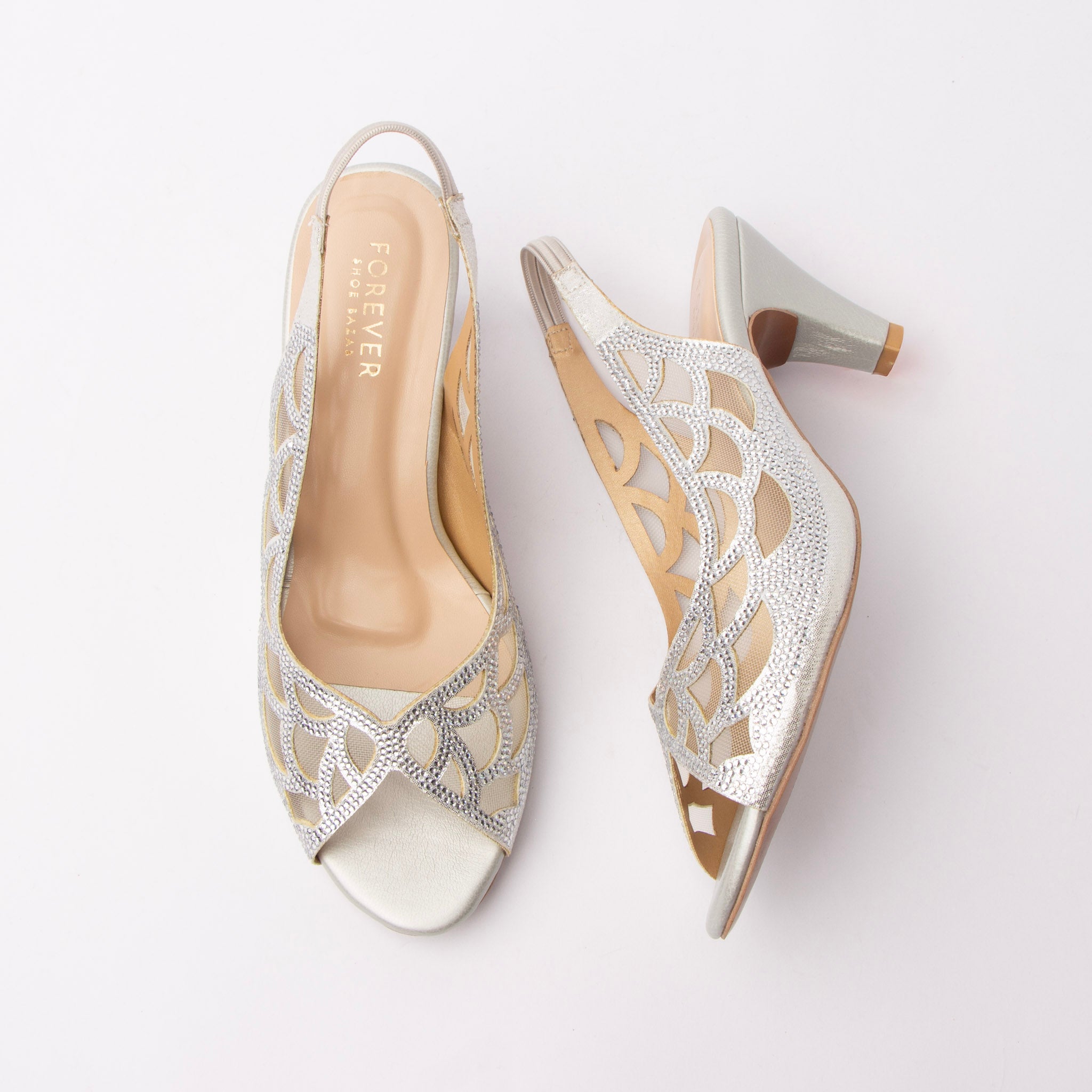 Silver embellished slingback pumps for women, clear silver rhinestones outline a scalloped petal motif over nude mesh insets on a shimmering silver upper, with laser-cut teardrops through the quarter, a gathered elastic slingback strap, a pearl-silver toe and footbed and a metallic silver flared cone kitten heel