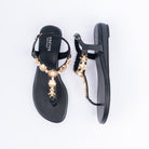 Black flat sandals for women, a run of gold seashell and starfish charms threaded with faux pearls down the T-strap, a slim buckled backstrap, and a cushioned footbed on a low sole