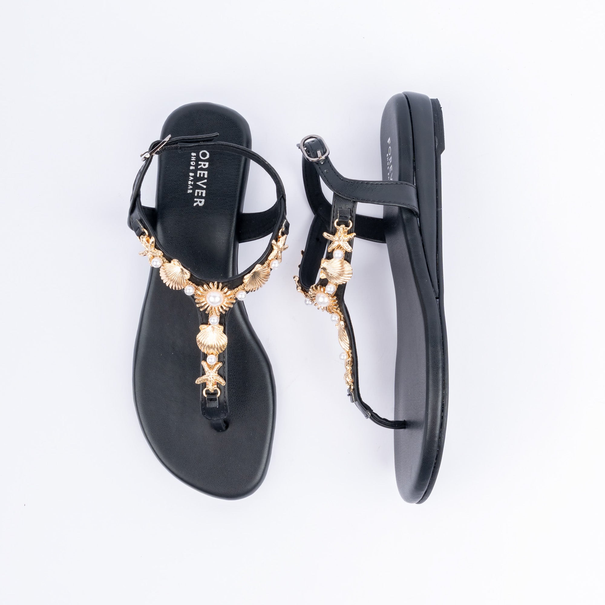 Black flat sandals for women, a run of gold seashell and starfish charms threaded with faux pearls down the T-strap, a slim buckled backstrap, and a cushioned footbed on a low sole